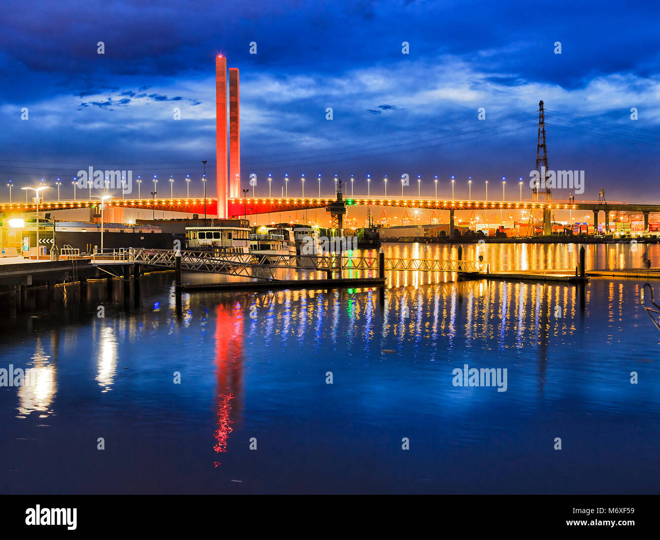 Colorato luminosamente illuminata Ponte del bullone a Melbourne Dockalns sobborgo oltre il fiume Yarra al tramonto che riflette ancora in acque contro il cielo blu scuro. Foto Stock