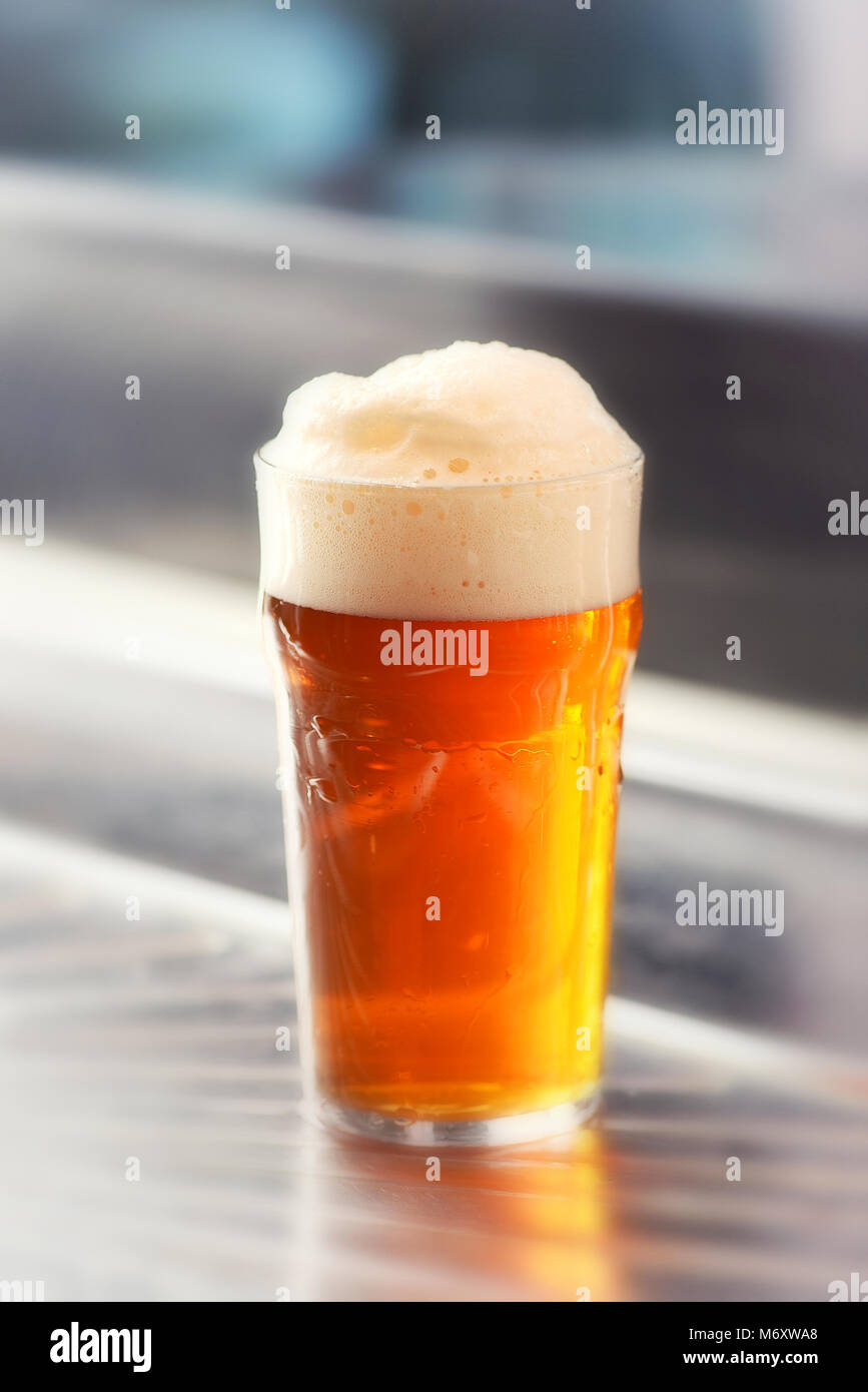 Servito fresco pinta di Spumeggiante birra alla spina con una buona testa in un vetro su una barra metallica contatore in un vicino la vista laterale Foto Stock