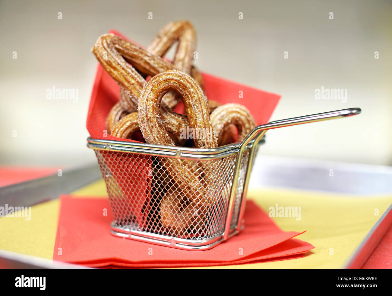 Cestello in filo metallico di croccanti dolci churros rivestito in una miscela di cannella e zucchero servito con un rosso tovagliolo di carta in un ristorante Foto Stock