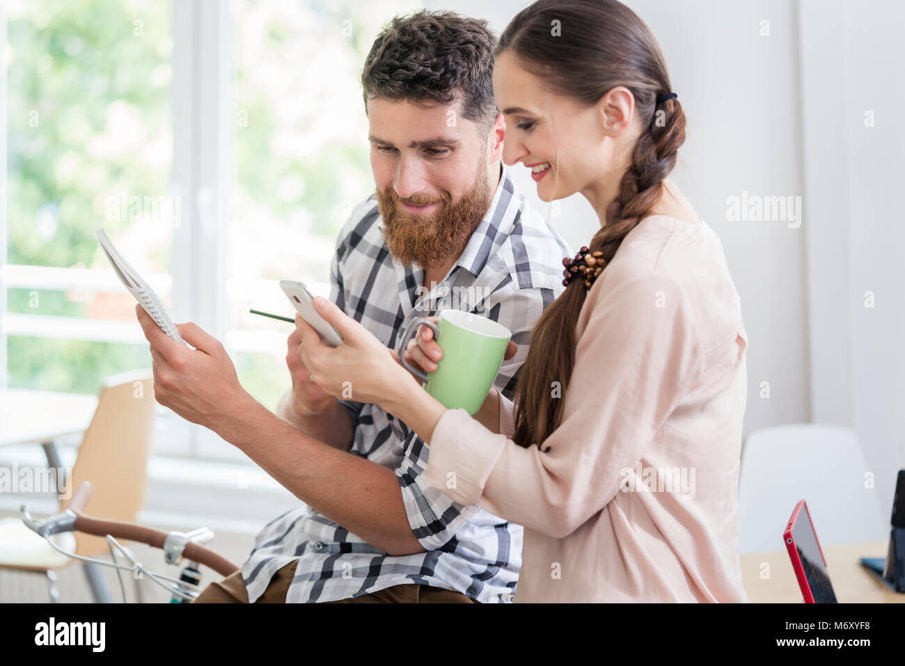 Due co-lavoratori sorridenti mentre si guarda un video sul cellulare Foto Stock