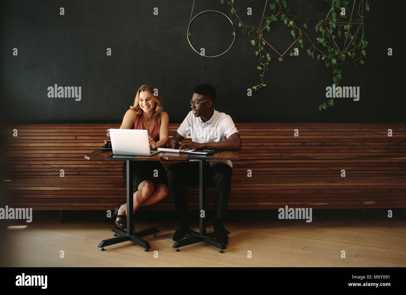 I partner aziendali in un coffee shop lavorando su un computer portatile. Amici seduti a un tavolo da caffè con laptop e taccuini facendo il lavoro. Foto Stock