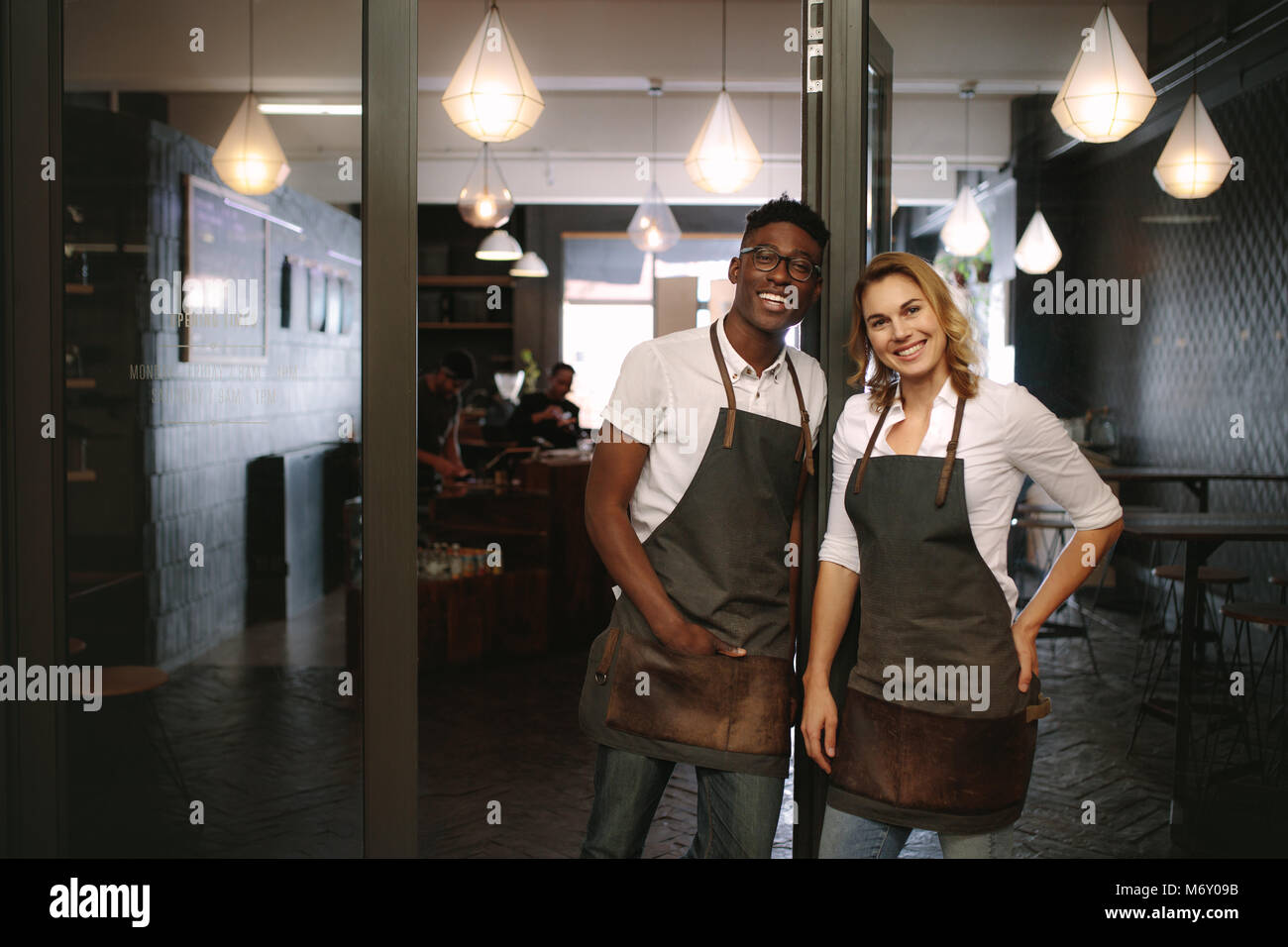 Caffè felice proprietario di un negozio di coppia permanente al loro negozio. L uomo e la donna baristi permanente al loro café indossando il grembiule. Foto Stock