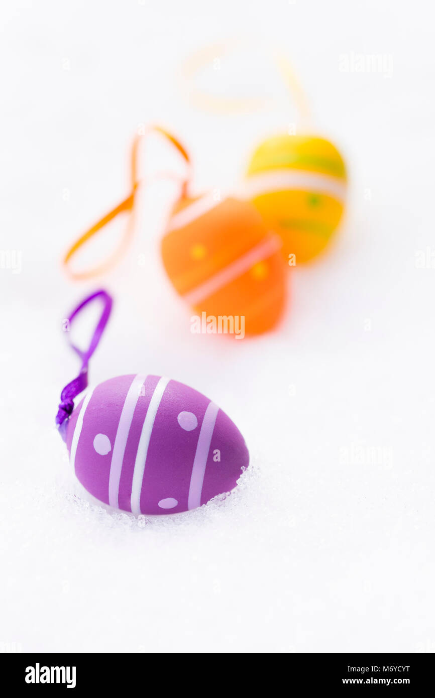 Primo piano della viola, l'arancione e giallo le uova di pasqua con nastri e decorate con righe e punti posa all'aperto sulla neve fresca in primavera Foto Stock