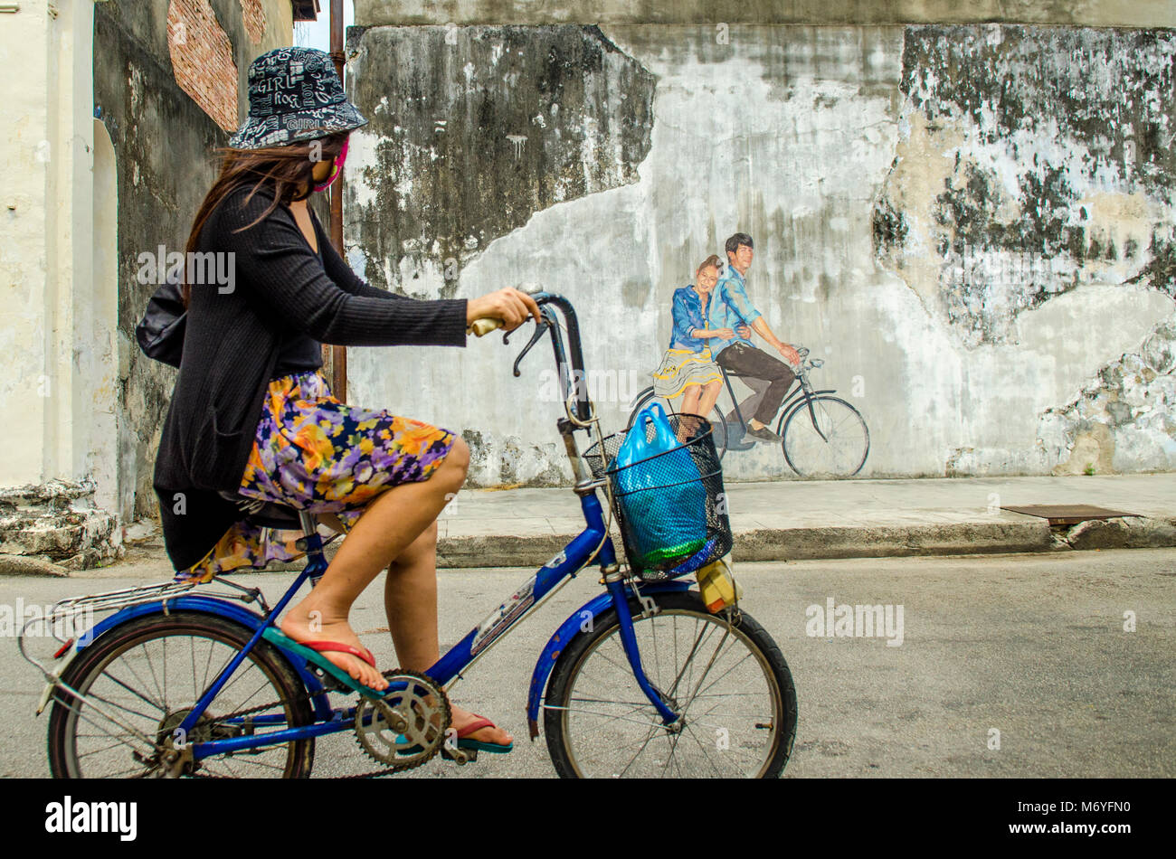 Ragazza sulla bicicletta pedalando passato Penang street art Foto Stock