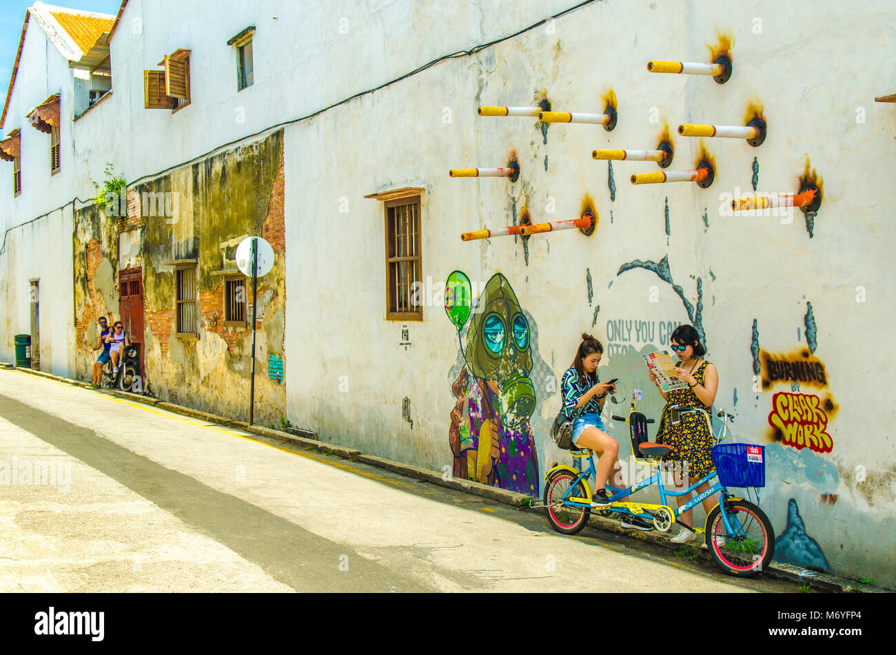 Ragazza sulla bicicletta pedalando passato Penang street art Foto Stock