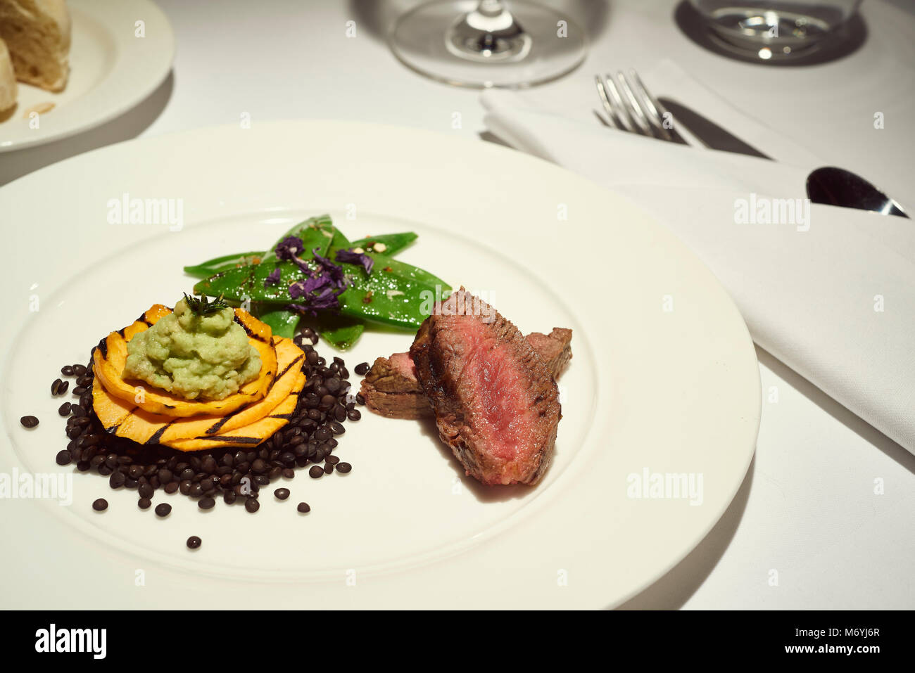 La cena a base di carne di manzo su un bianco puro piastra cena con pane e acqua e vino Foto Stock