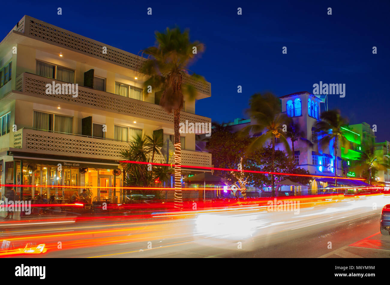 Ocean Drive a Miami la notte con vivaci colori di strada. Auto passando per la creazione di linee di luce durante una lunga esposizione. Le palme, hotel in background. Foto Stock