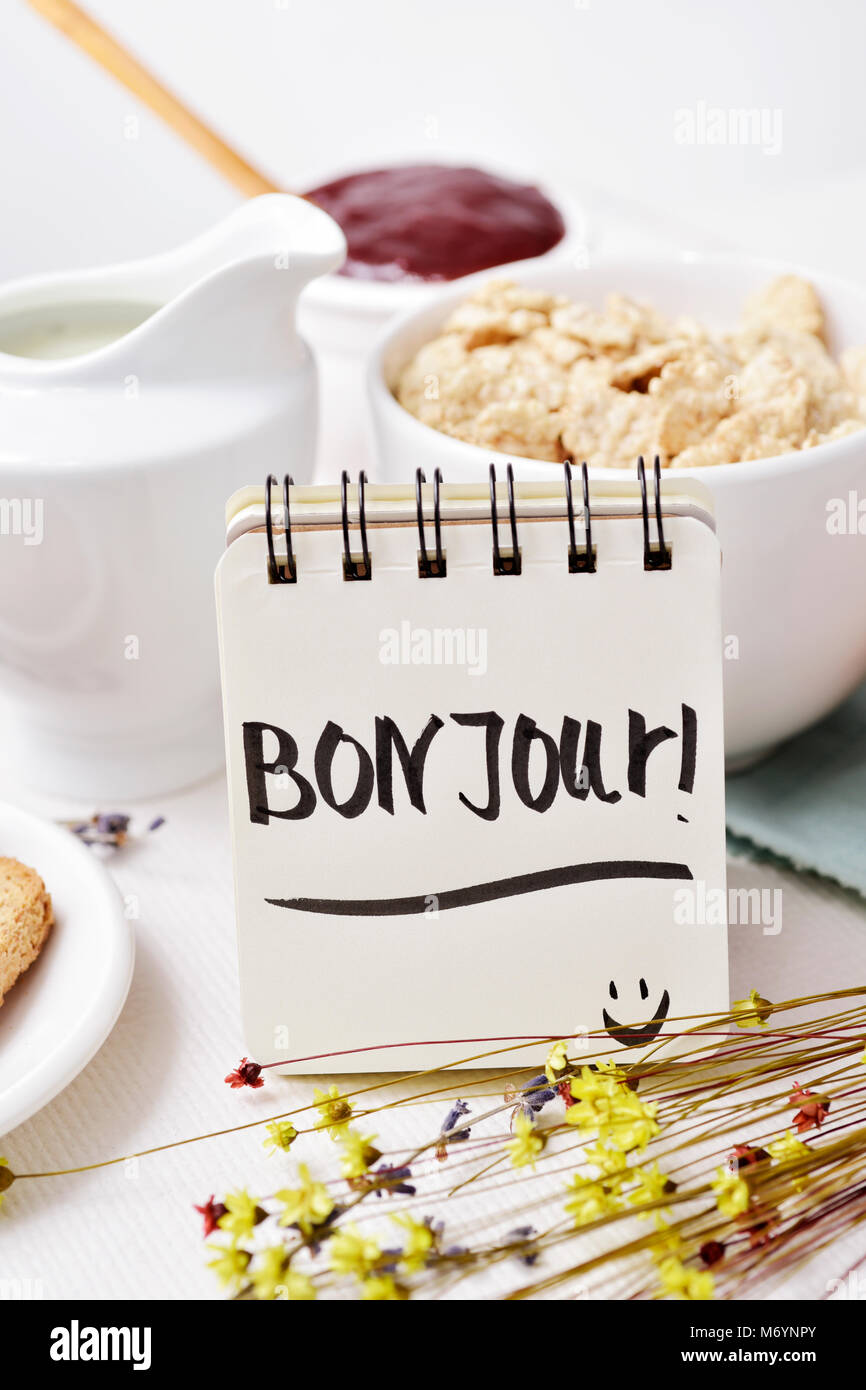 Primo piano di un tavolo per la prima colazione con un vaso di porcellana con cereali, qualche toast, una ciotola con marmellata e una nota con il testo bon jour, buongiorno Foto Stock