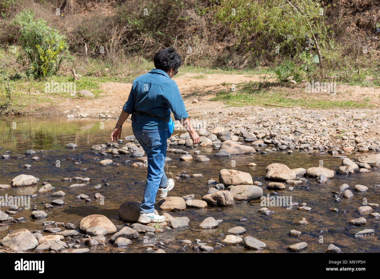 Oaxaca, Messico - Una donna messicana attraversa un ruscello mentre escursionismo in Occidente Etla Valle di Oaxaca rurale. Ella è parte di un gruppo chiamato Hoofing In Oa Foto Stock