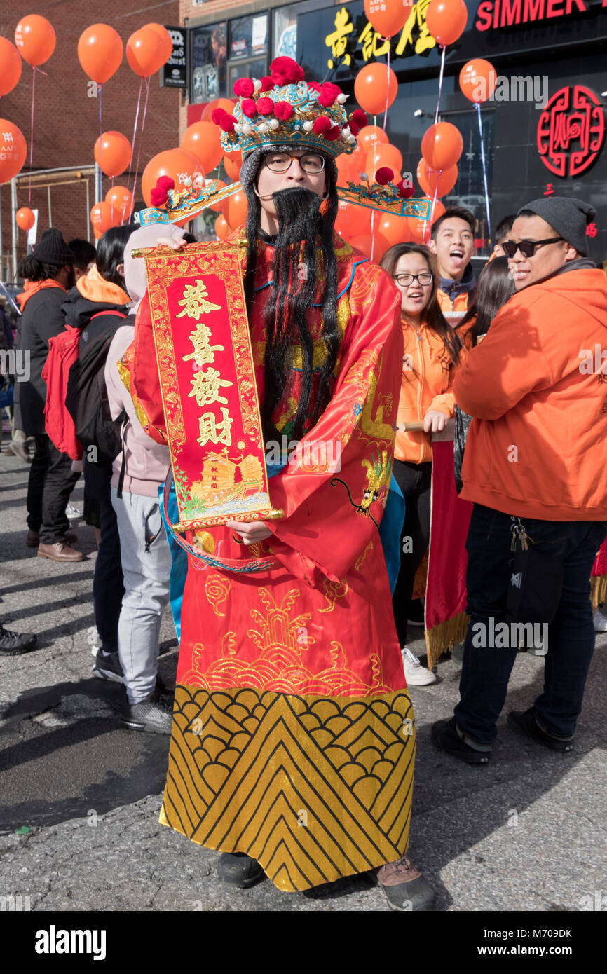 Un giovane cinese uomo americano in un costume tradizionale detiene un banner con un nuovo anni saluto al nuovo anno sfilano in Chinatown, Lavaggio Queens NY Foto Stock