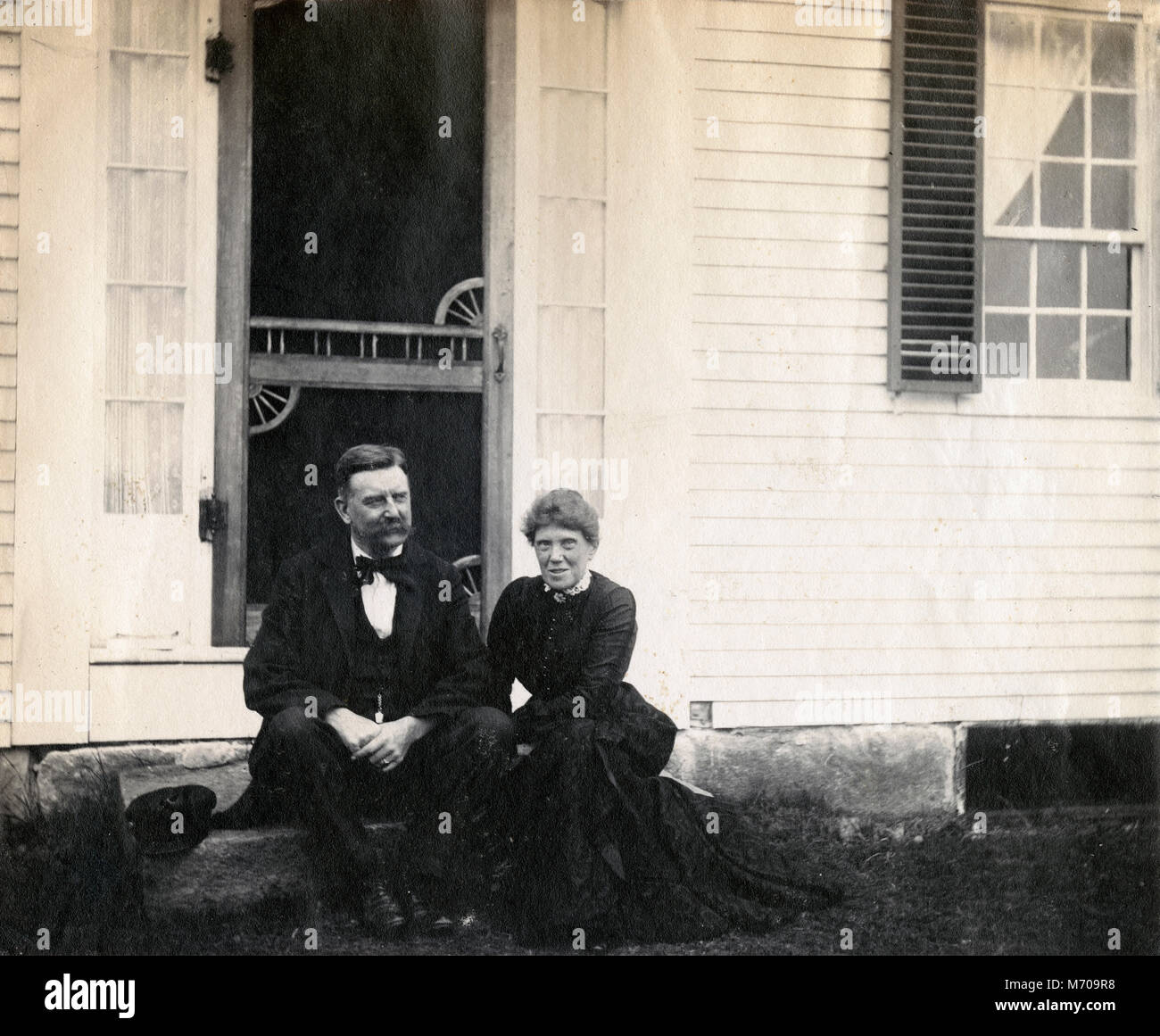 Antique circa 1905 fotografia, coppia di anziani seduti sul gradino anteriore della casa. La posizione è in o vicino a Riggsville (ora Robinhood), Maine in Sagadahoc County, Stati Uniti d'America. Foto Stock