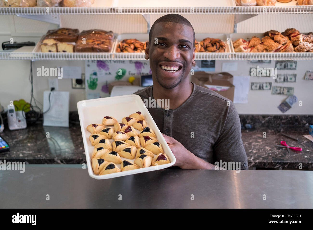 Un giovane baker e il panificio negozio proprietario visualizza il Purim hummentaschen egli cotta nel suo bakery & cafe in Pleasantville, New York. Foto Stock