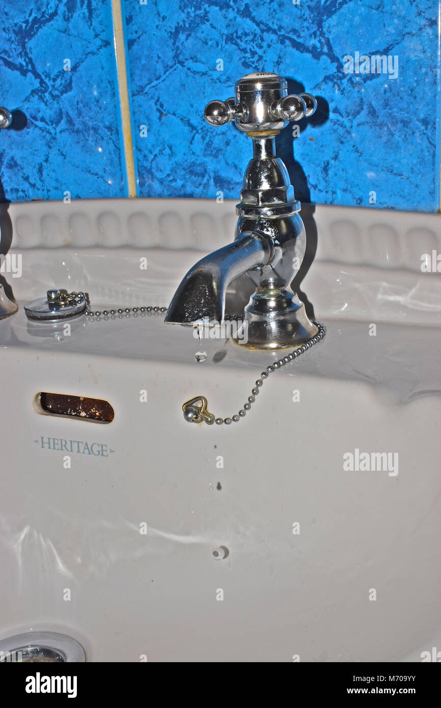 Gocciolamento di acqua da un rubinetto bagno a causa di un usurato la rondella. Acqua per i rifiuti verso il basso del lavandino. Foto Stock