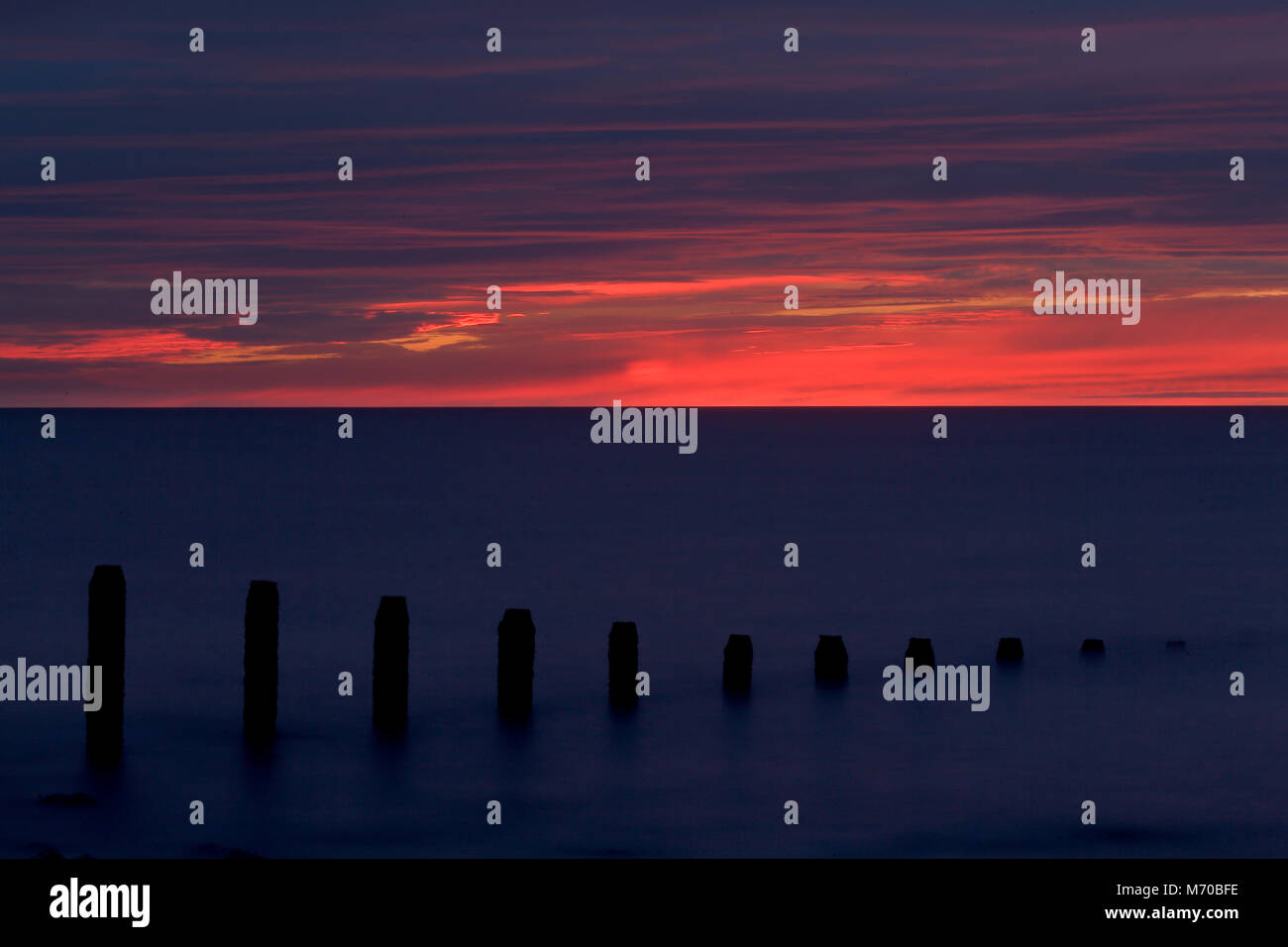 Linea di pennelli in mare al tramonto, costa del Galles Settentrionale Foto Stock