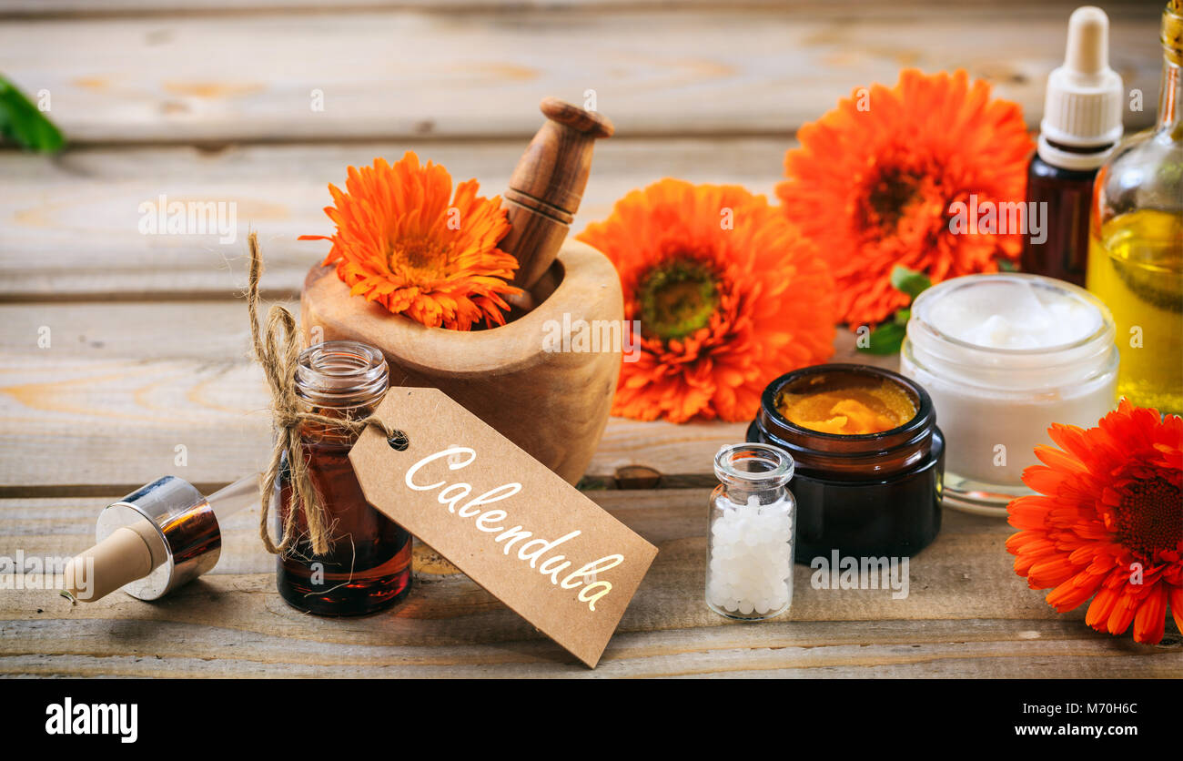 Calendula o fiorrancio prodotti. Olio essenziale, globuli di omeopatia e cosmetici, tag con testo calendula. Tavolo in legno sfondo Foto Stock