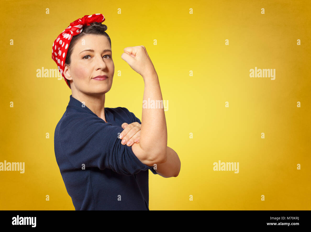 Sicuro di sé donna di mezza età con un pugno chiuso arrotolando il suo manicotto, spazio di testo, omaggio a icona americana Rosie chiodatrice Foto Stock