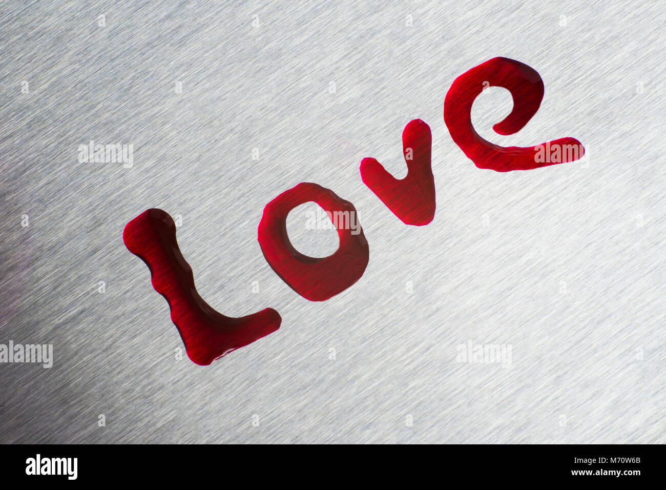 Gocce di colore rosso nella forma della parola amore. La superficie è metallico. Foto Stock