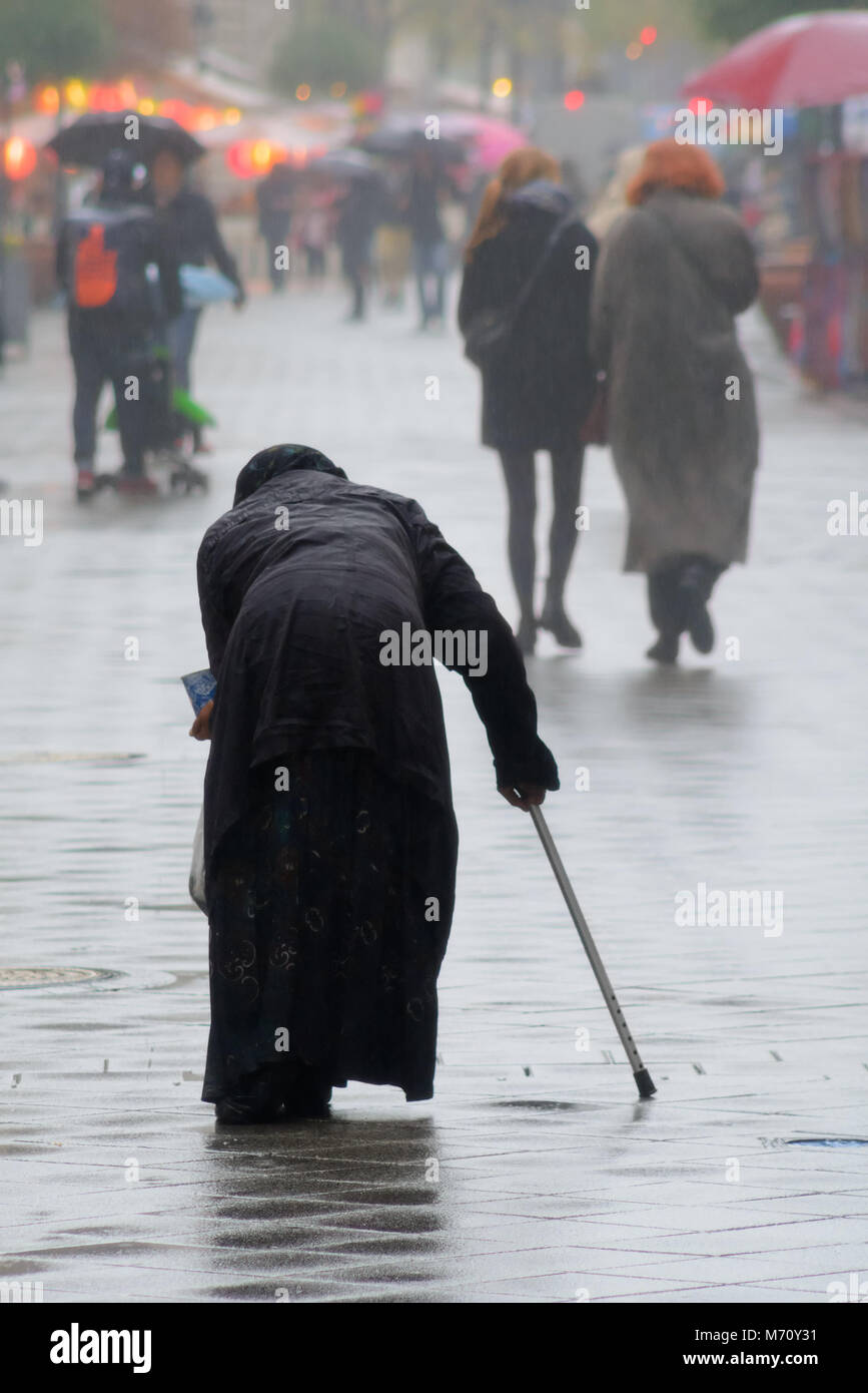 Il sambuco donna chiede elemosina sulla strada sotto la pioggia Foto Stock