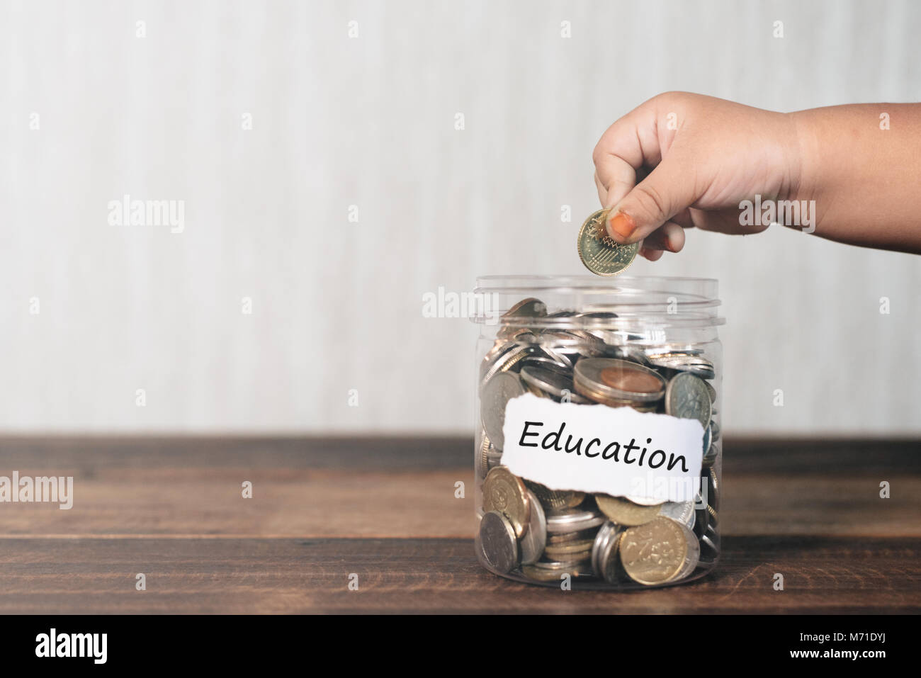Ritagliate la mano di un bambino mettendo moneta in vaso pieno di monete, il risparmio per il concetto di istruzione Foto Stock