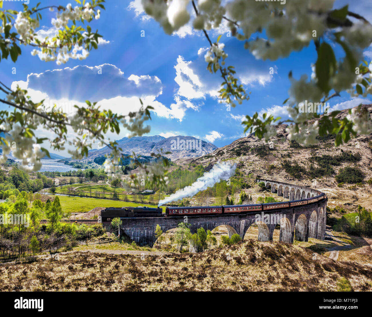 Glenfinnan viadotto ferroviario in Scozia con il vapore giacobita treno contro il tramonto sul lago Foto Stock