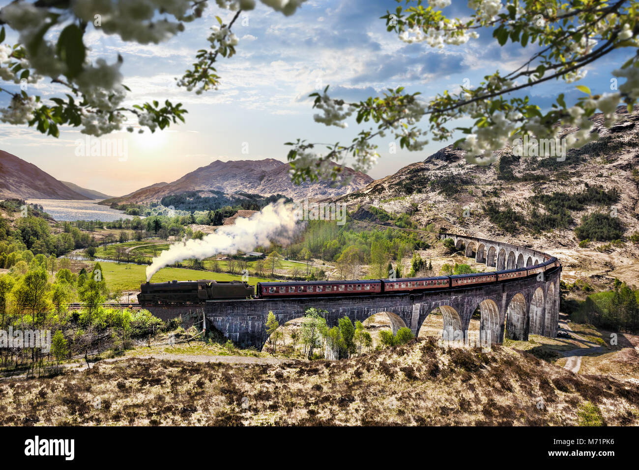 Glenfinnan viadotto ferroviario in Scozia con il vapore giacobita treno contro il tramonto sul lago Foto Stock