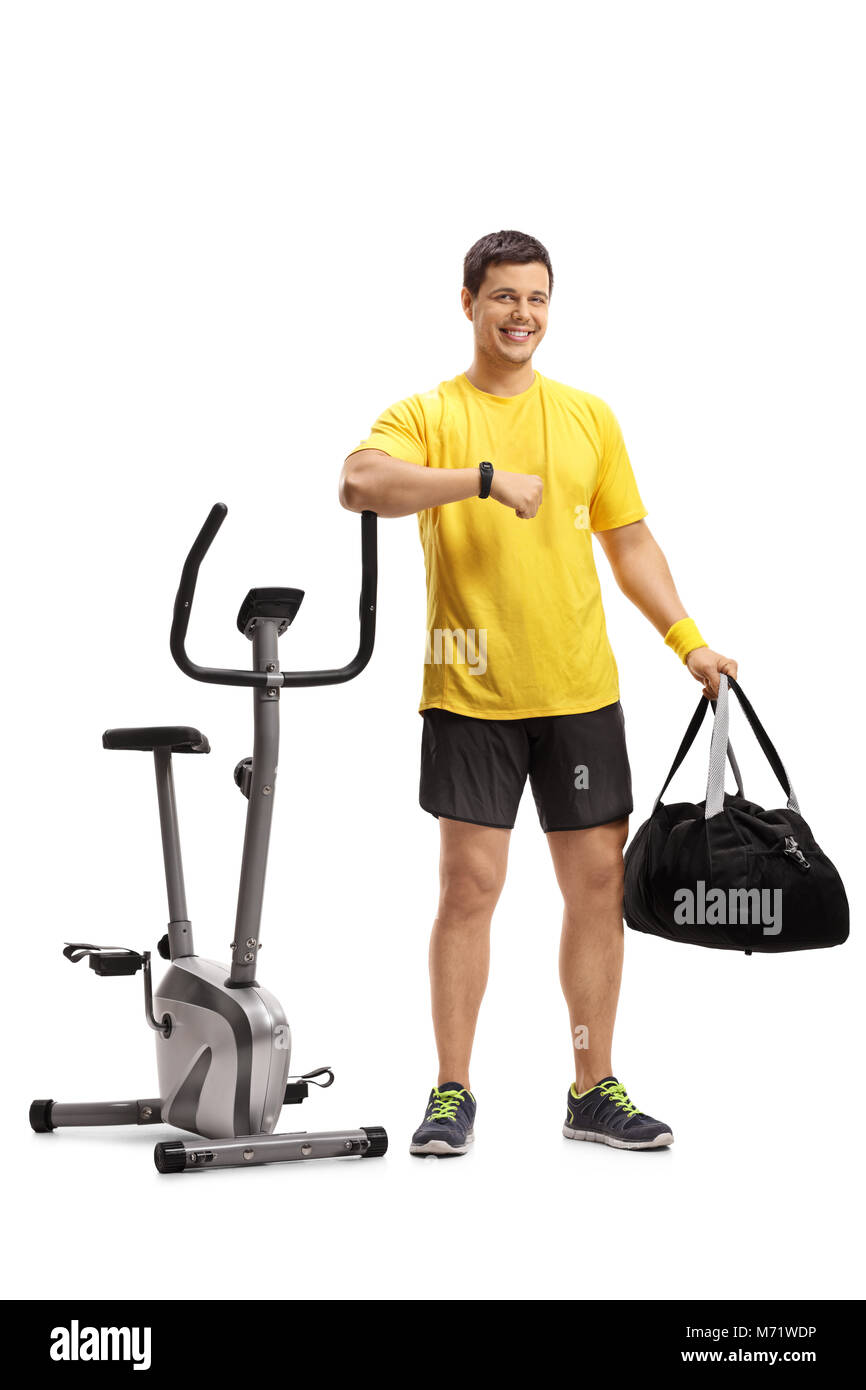 A piena lunghezza Ritratto di una giovane con una borsa sportiva appoggiandosi ad una cyclette isolati su sfondo bianco Foto Stock