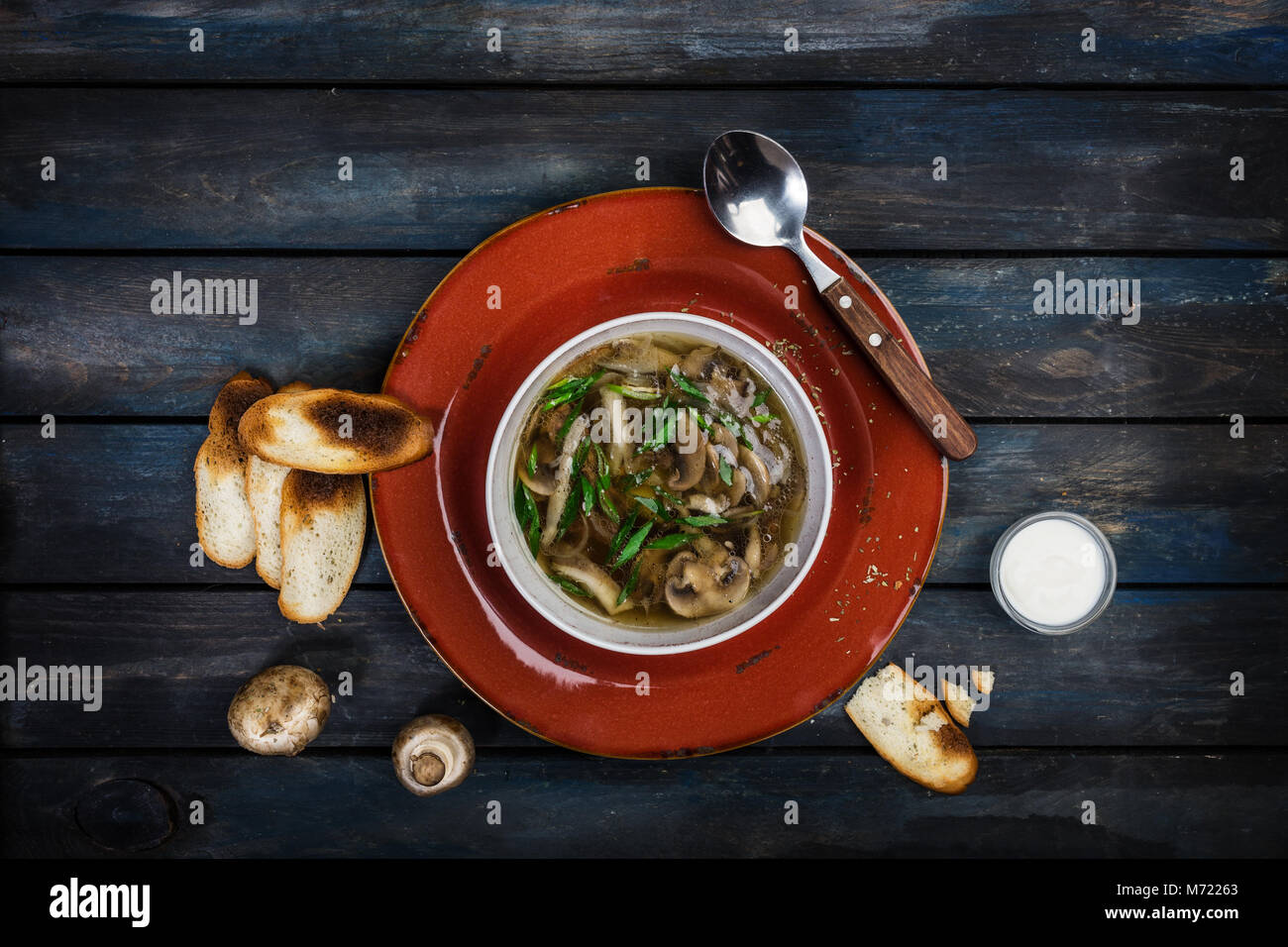 Fresca zuppa di funghi con cipolla verde la panna acida e il pane di patatine con un cucchiaio. Su una piastra di ceramica. Colore sfondo di legno. Vista superiore Foto Stock