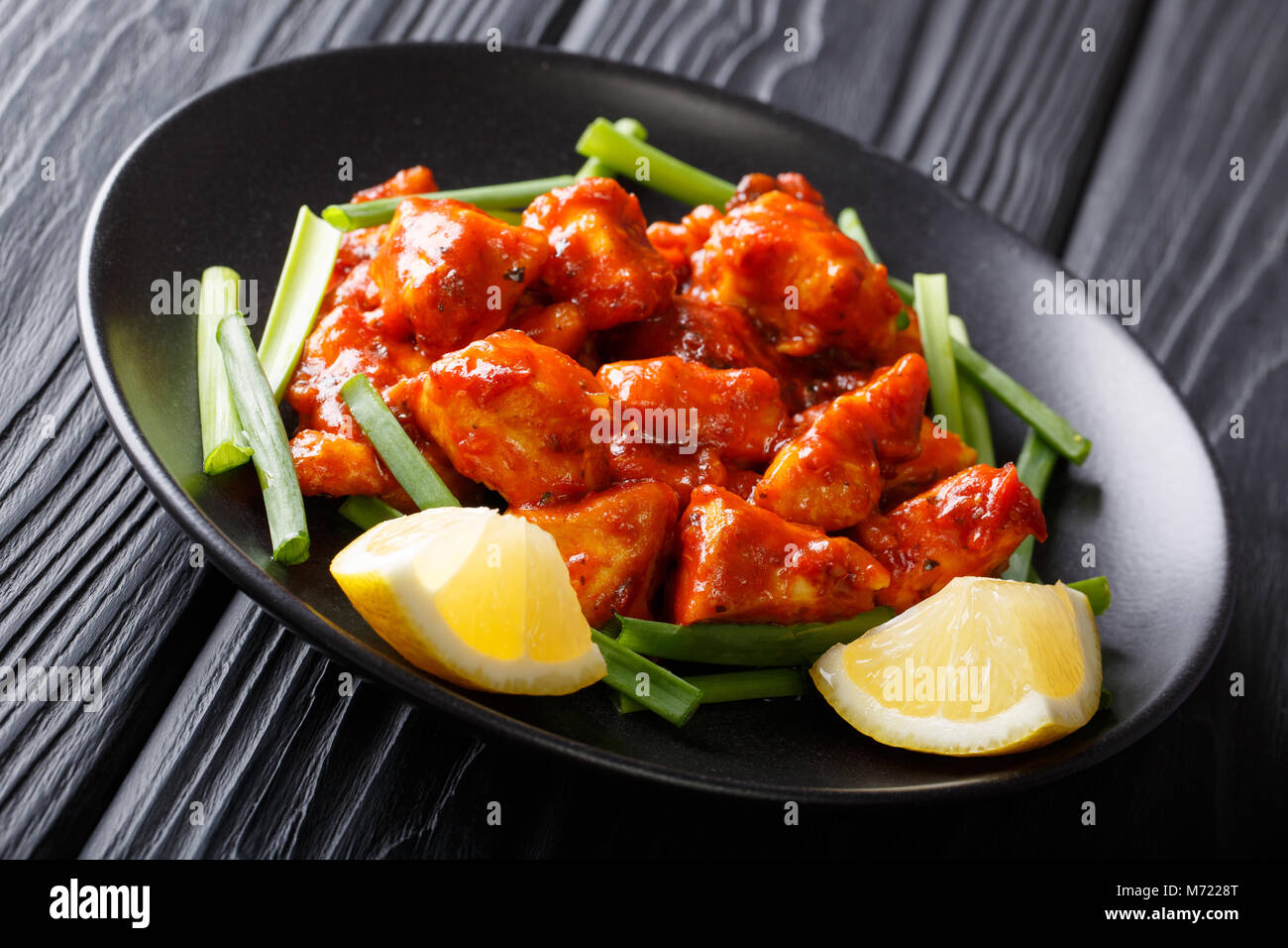 Piccante di pezzi di pollo in salsa rossa con le cipolle verdi e limone close-up su una piastra su un piano orizzontale. Foto Stock