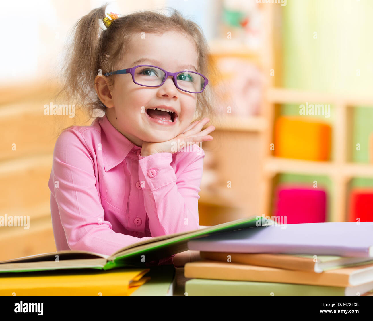 Smart kid in bicchieri la lettura di libri seduti al tavolo in camera sua Foto Stock