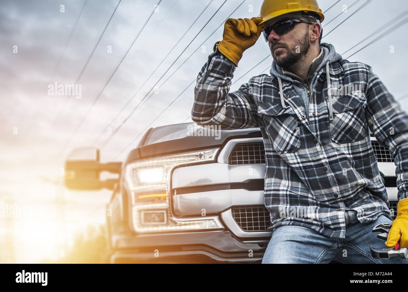 Imprenditore caucasico lavoratore nel Casco giallo e giallo guanti di sicurezza nella parte anteriore del suo pickup. Tema di costruzione. Foto Stock