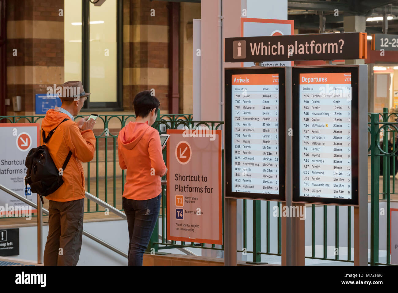 Le persone che usano telefoni intelligenti a un treno scheda indicatore a Sydney la Stazione Centrale Foto Stock