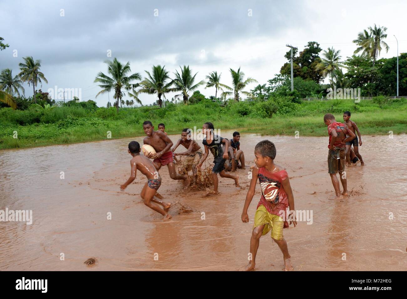 I bambini giocare a rugby in un mudbath al di fuori di un villaggio di campagna di Figi. Heavy Rain aveva invaso il loro campo da gioco ma questo non ha fermato il loro amore per il rugby. La loro gioia e la loro esuberanza è normale vedere in una comunità che è estremamente povero. Foto Stock