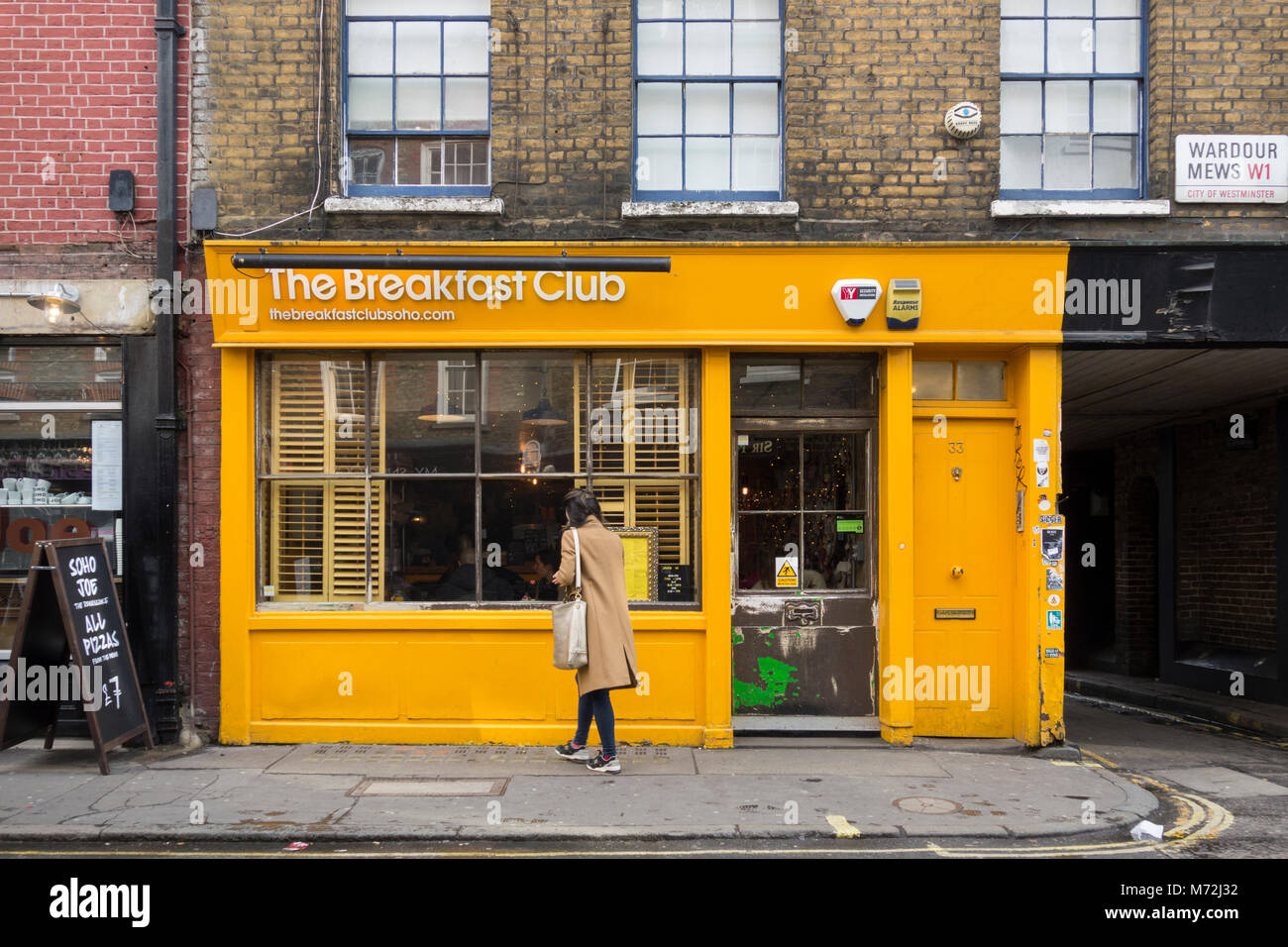 Una donna che guarda al Breakfast Club giallo brillante, D'Arblay Street, Soho, Londra, W1, Inghilterra, Regno Unito Foto Stock