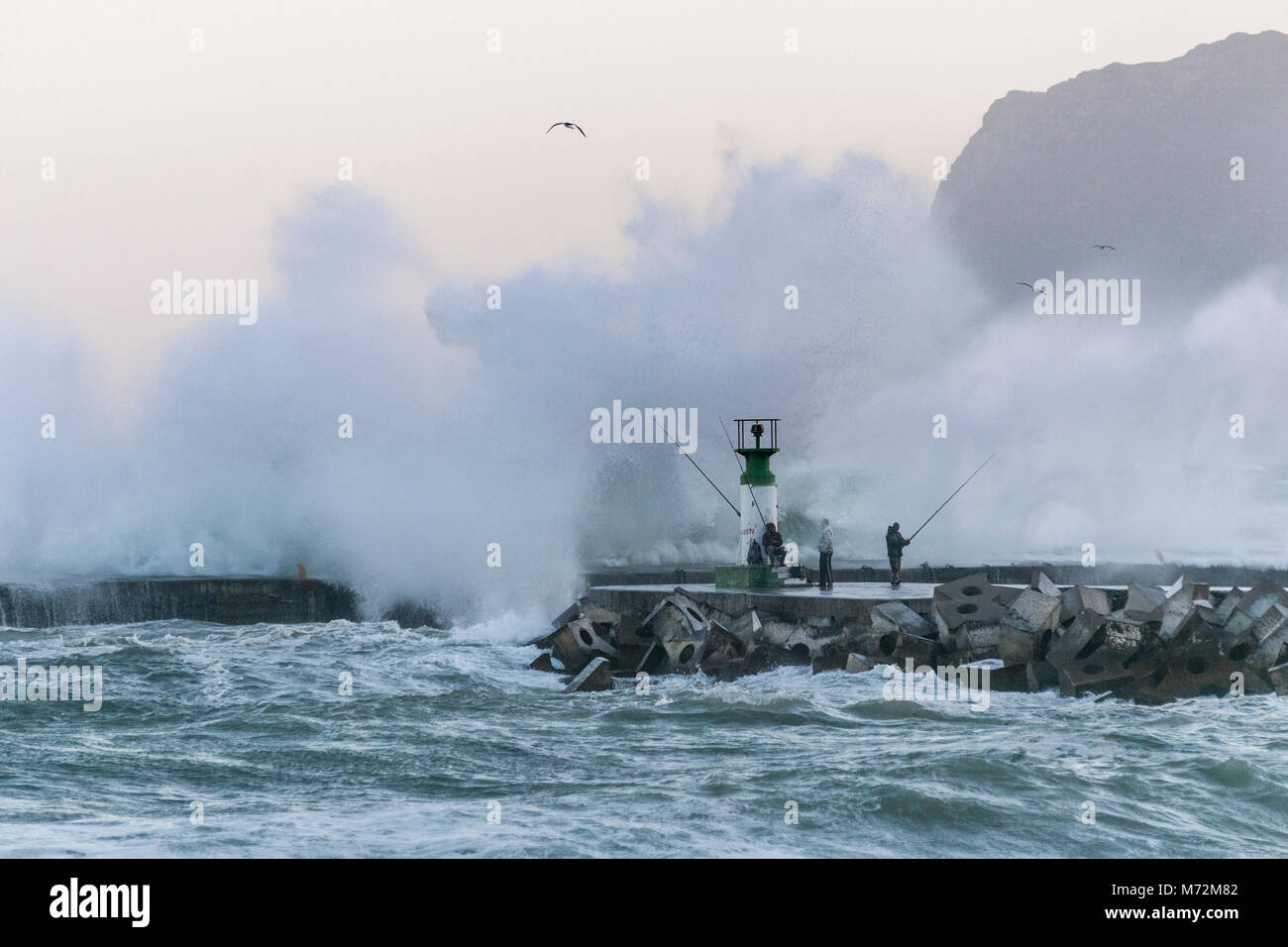 I pescatori sfidando le onde enormi che si sono visti qui di schiantarsi contro il frangiflutti di Kalk Bay Harbor in Cape Town, Sud Africa. Foto Stock