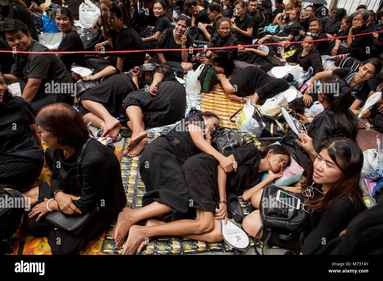 Due donne dormire e abbracciando ogni altro in strada tra una folla di persone in abiti neri, aspettando il Royal cremazione in Sanam Luang Foto Stock