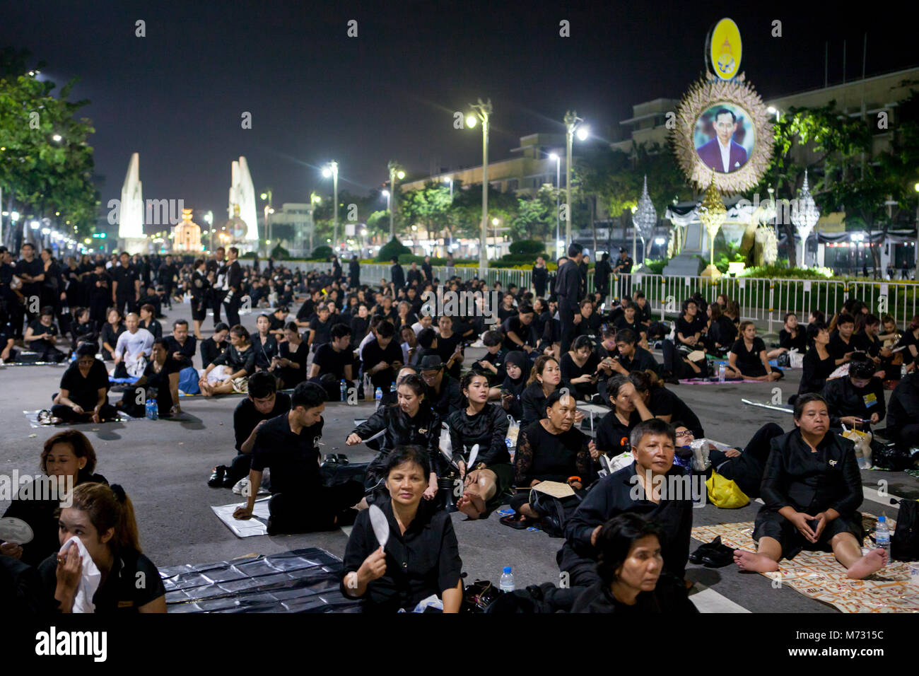 La gente che indossa abiti neri in seduta Ratchadamnoen Road dopo la royal cremazione, in cui la democrazia è un monumento in background in Bangkok Foto Stock