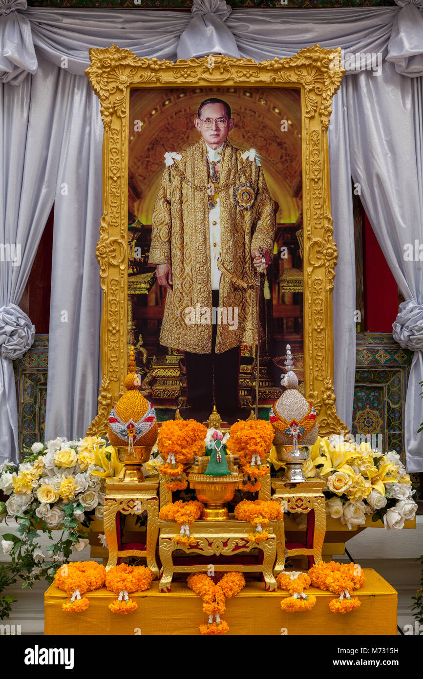 Gigante immagine incorniciata di Re Bhumibol Adulyadej Rama IX, circondato da drappi dietro un altare con arancia e fiori di colore giallo Foto Stock