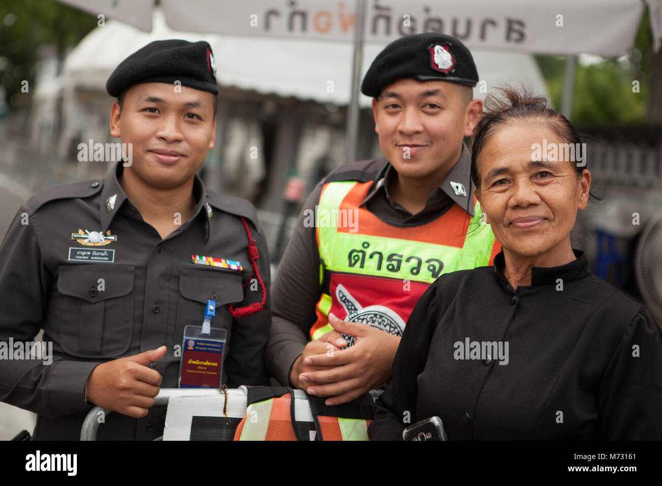 Due soldati tailandesi e una donna che indossa il lutto vestito nero, sorridente alla telecamera, il giorno dopo la cremazione reale Foto Stock