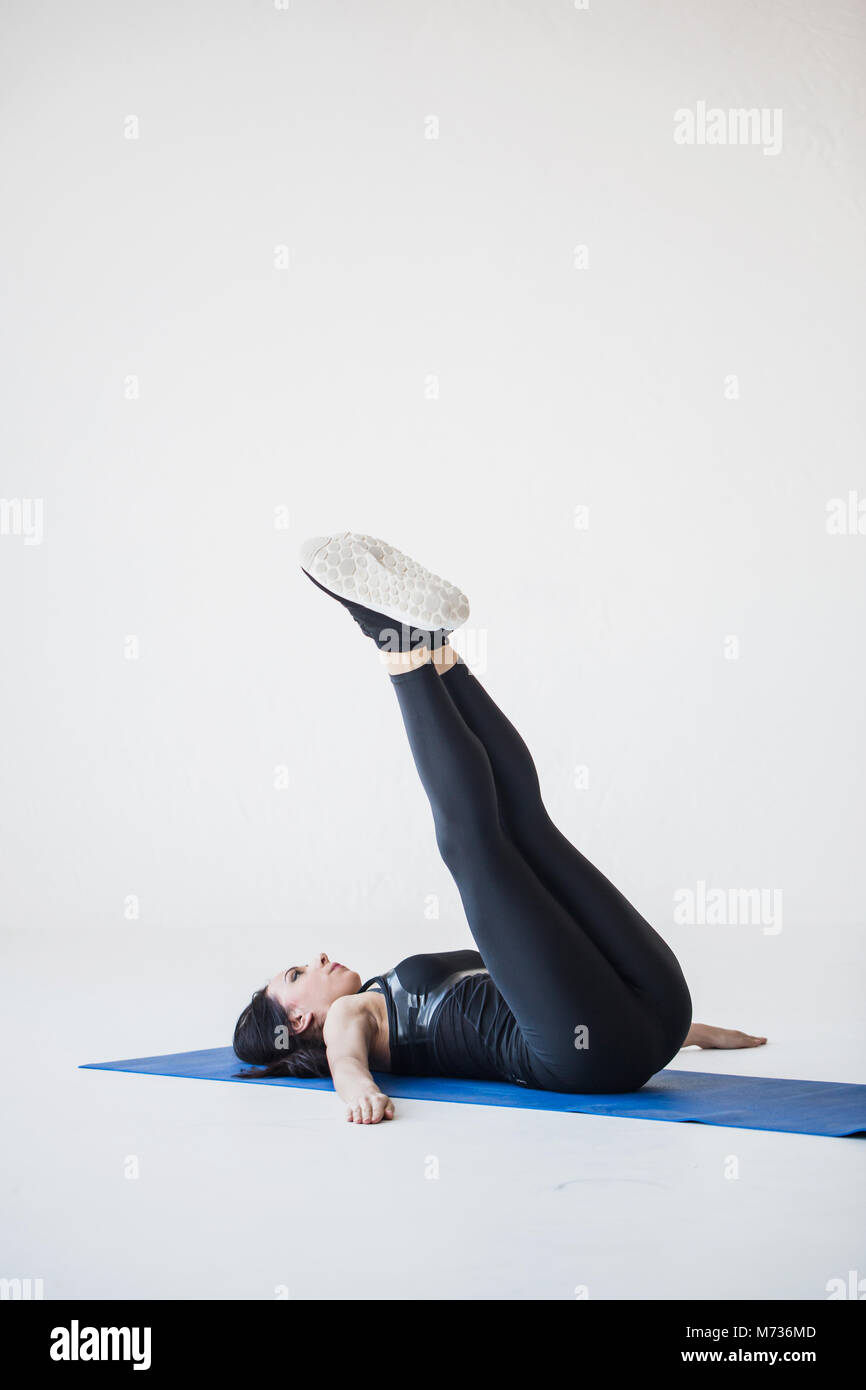 Photo tutorials per lo sport i principianti. L'atletica brunette trainer è sdraiato sul tappeto di esercizio e facendo retromarcia twist crunch. Foto Stock