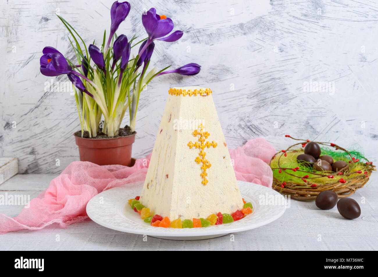 Cagliata tradizionale torta di Pasqua con frutta candita e uova di cioccolato, fiori di primavera crocus sulla vacanza sfondo luminoso. Pasqua cottage cheese dess Foto Stock