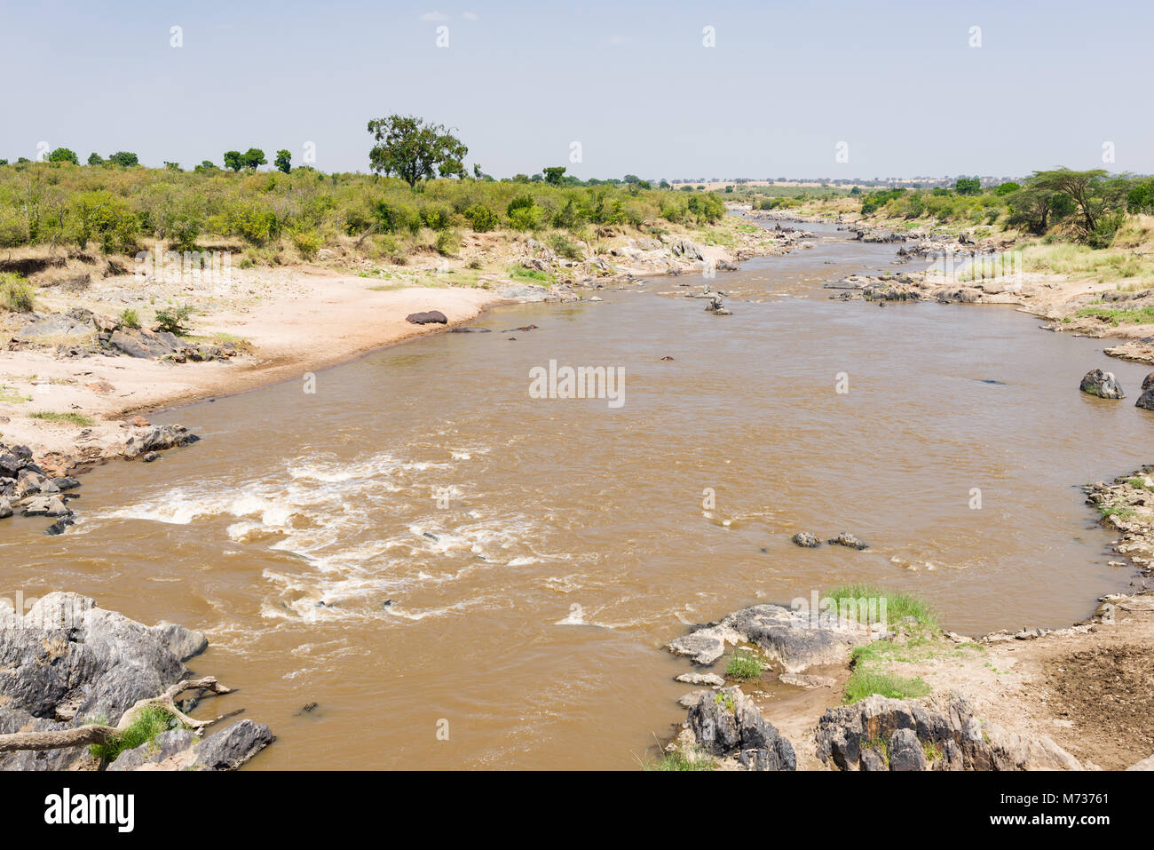 Il fiume di Mara che fluisce nel Maasai Mara riserva nazionale, le rocce e la vegetazione in linea le sponde in una giornata di sole, Kenya Foto Stock