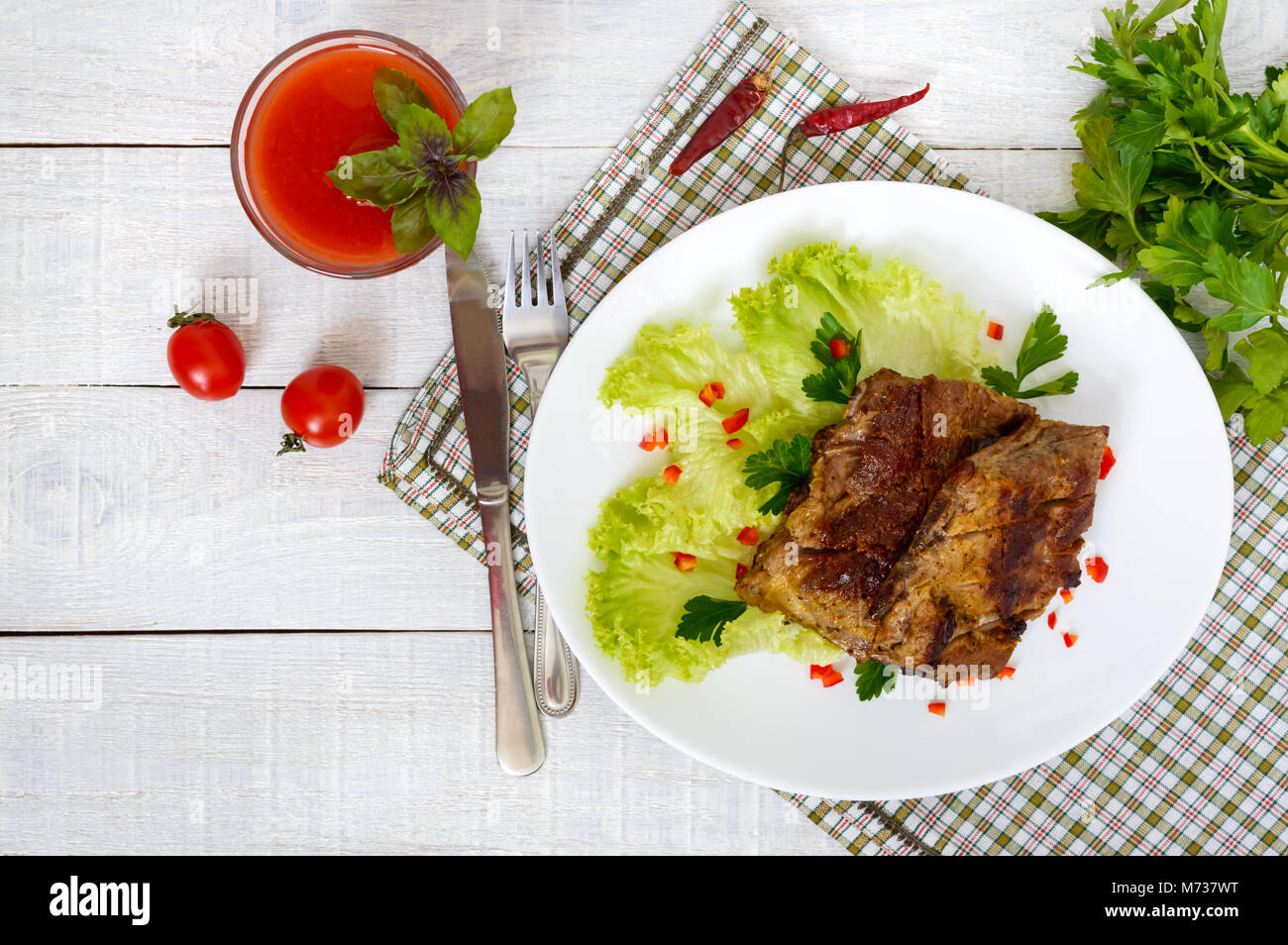 Maiale fritto nervature su una piastra con verdi e il succo di pomodoro su un bianco sullo sfondo di legno. Foto Stock