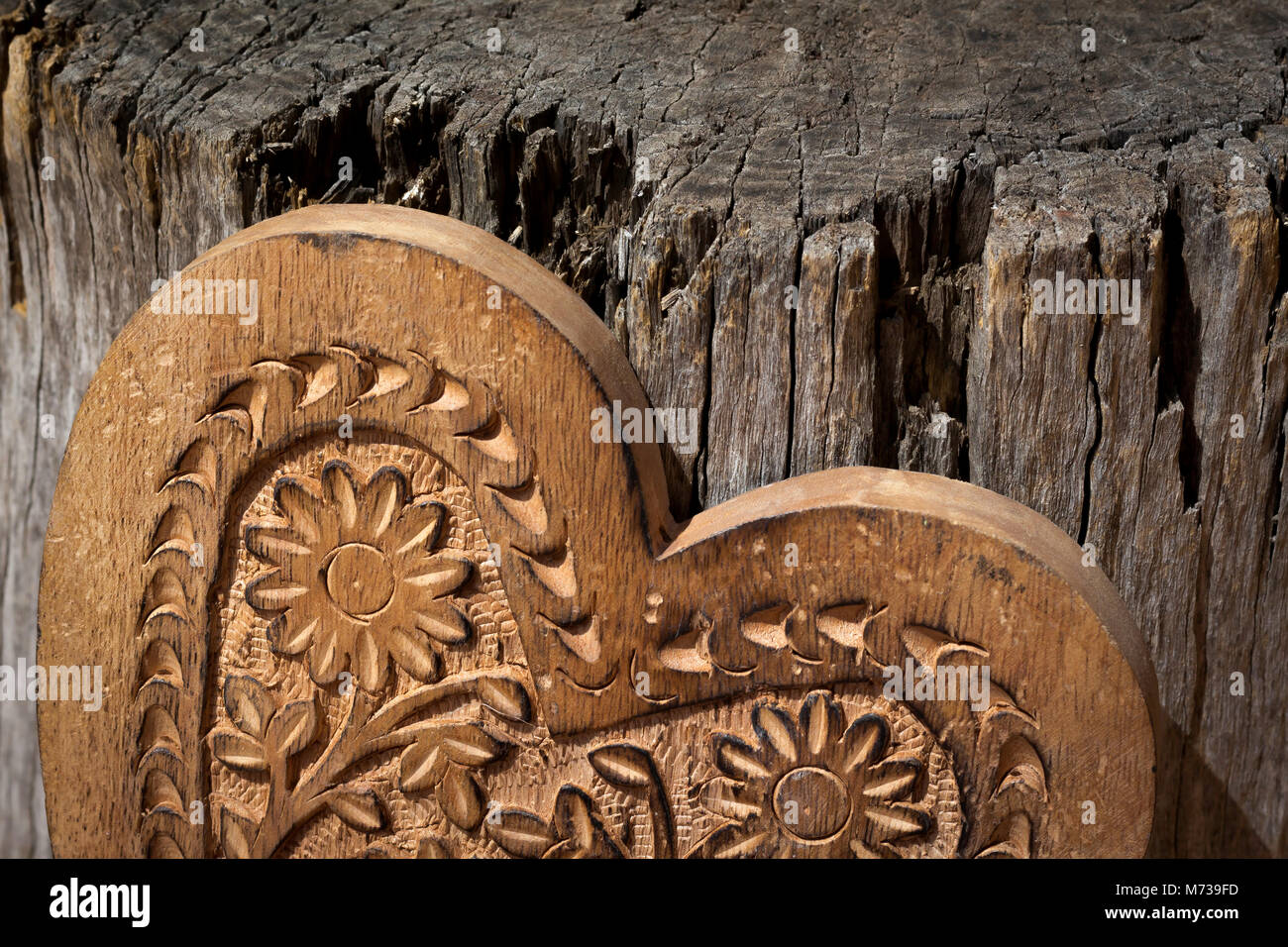 La metà superiore di un cuore di legno con motivi floreali ha voluto in essa con un vecchio ceppo di albero in background, il cuore è leggermente inclinata verso destra Foto Stock