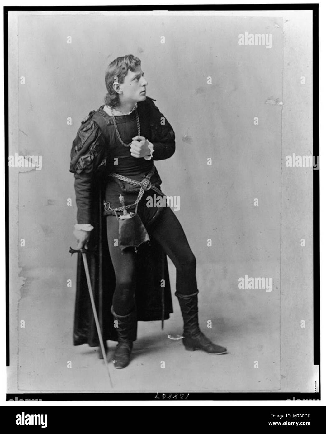 Questo ritratto a figura intera di Creston Clarke lo mostra in piedi e in mano una spada, raffigurando il suo ruolo di personaggio in un'opera teatrale. L'immagine si concentra sul costume teatrale e sulla postura. Foto Stock