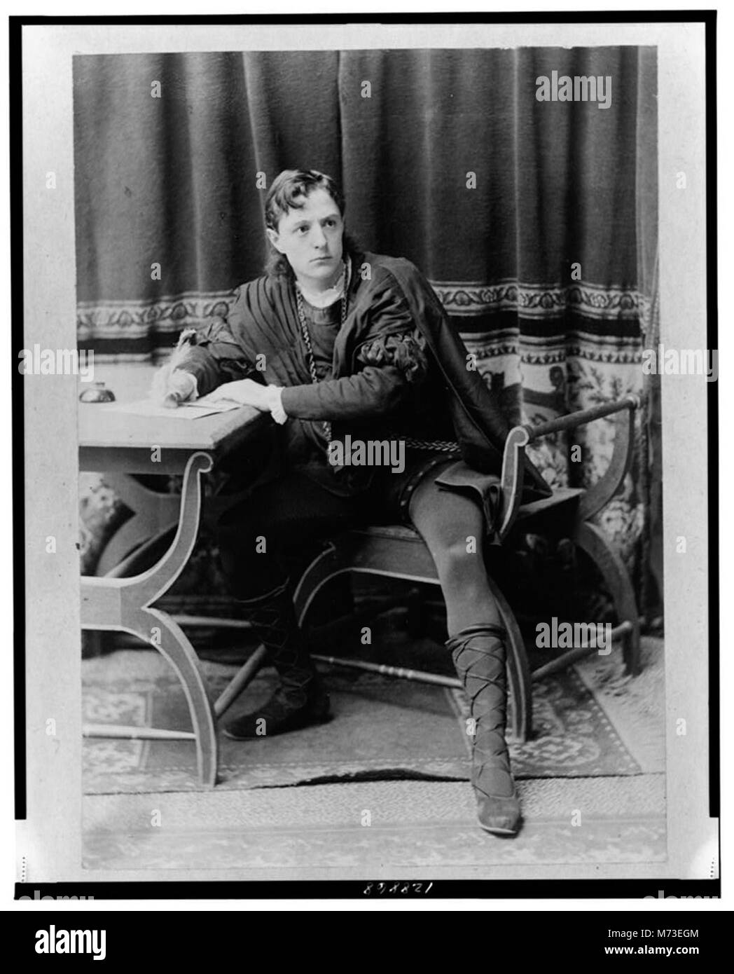 Un ritratto a figura intera di Creston Clarke, seduto a una scrivania, scrivendo con una penna quill mentre ritrae un personaggio in un'opera teatrale. L'immagine enfatizza il suo abbigliamento, la postura e l'ambientazione. Foto Stock