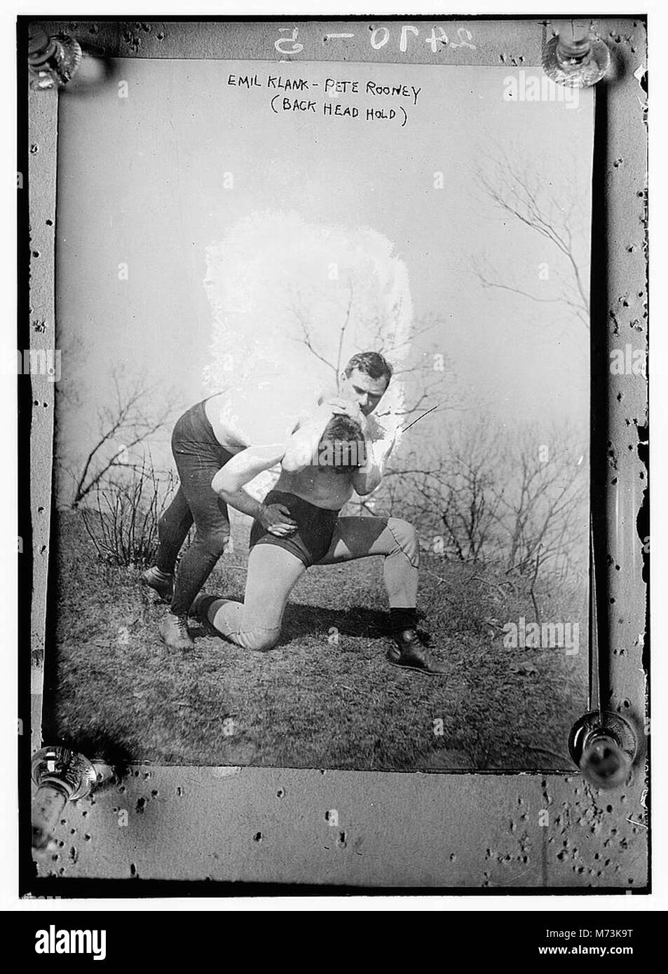 Questa immagine mostra Emil Klank che tiene Pete Rooney in un headlock alla schiena durante un match di wrestling. La fotografia cattura un momento di un evento di wrestling professionistico, mostrando l'atletismo e l'intensità dello sport. Foto Stock