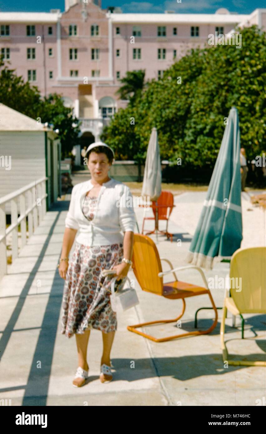 Una donna che indossa un vestito e un maglione pone tenendo un portamonete bianco, 1955. () Foto Stock