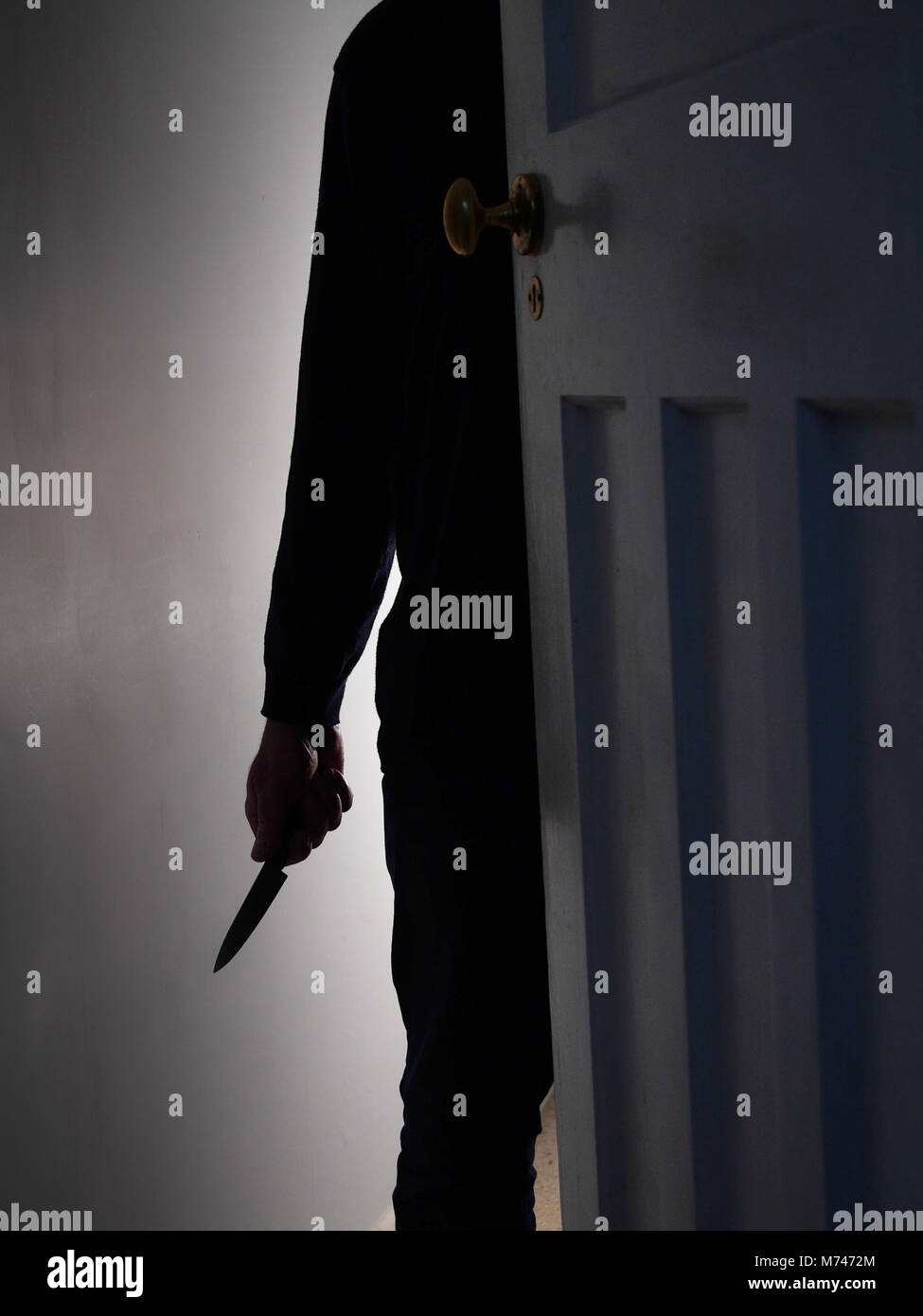 Silhouette di un irriconoscibile uomo con coltello cercando minacciando il vano di una porta Foto Stock