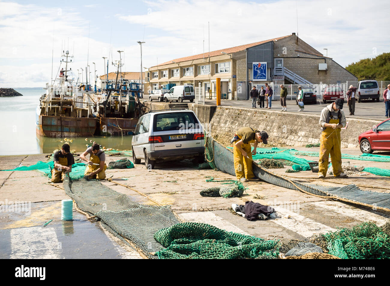 I pescatori a ricucire le reti nel porto di La Cotiniere sull'isola di Oleron, Francia, con barche da pesca ormeggiate di fronte al mercato del pesce edificio. Foto Stock