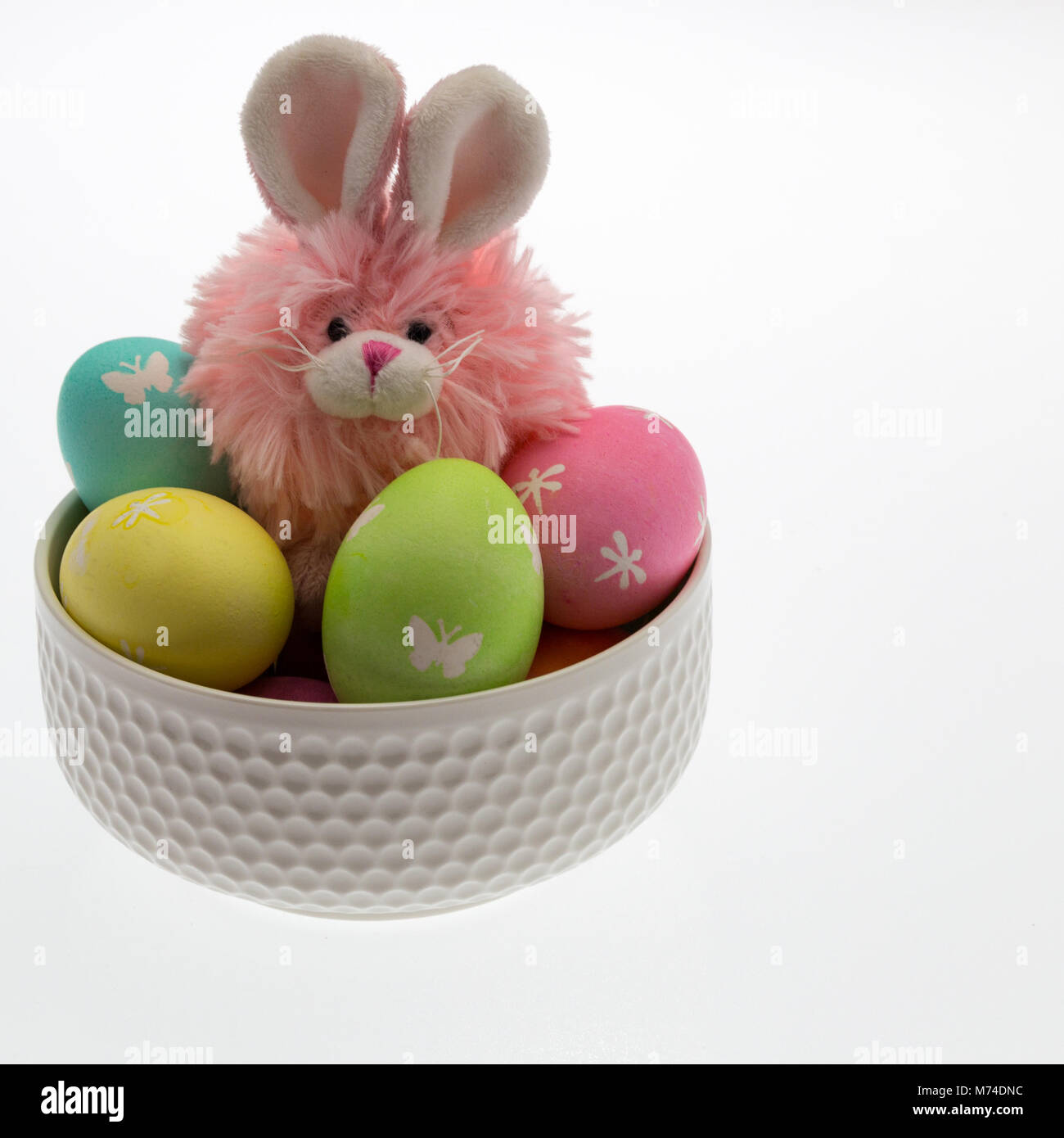 Rosa coniglietto di pasqua, giallo pulcino e numerosi mano uova tinte pastello con carta colorata sminuzzare in una ciotola bianco di convogliare una Pasqua tema per bambini. Foto Stock